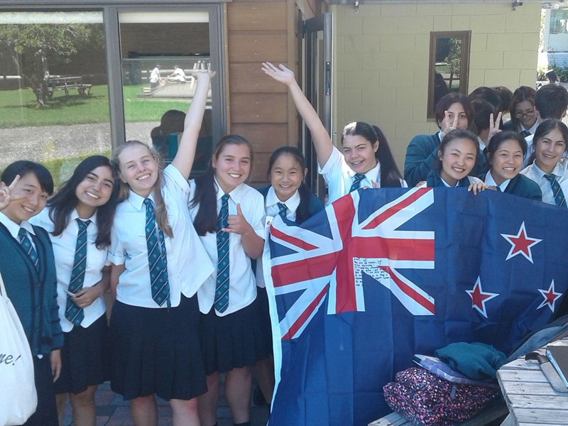 Group of cheerful students in uniforms holding the new zealand flag